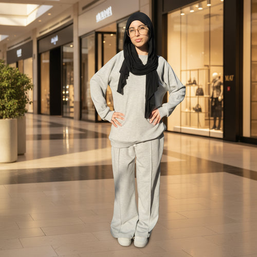 Person wearing a gray outfit with a black hijab standing outdoors in a mall