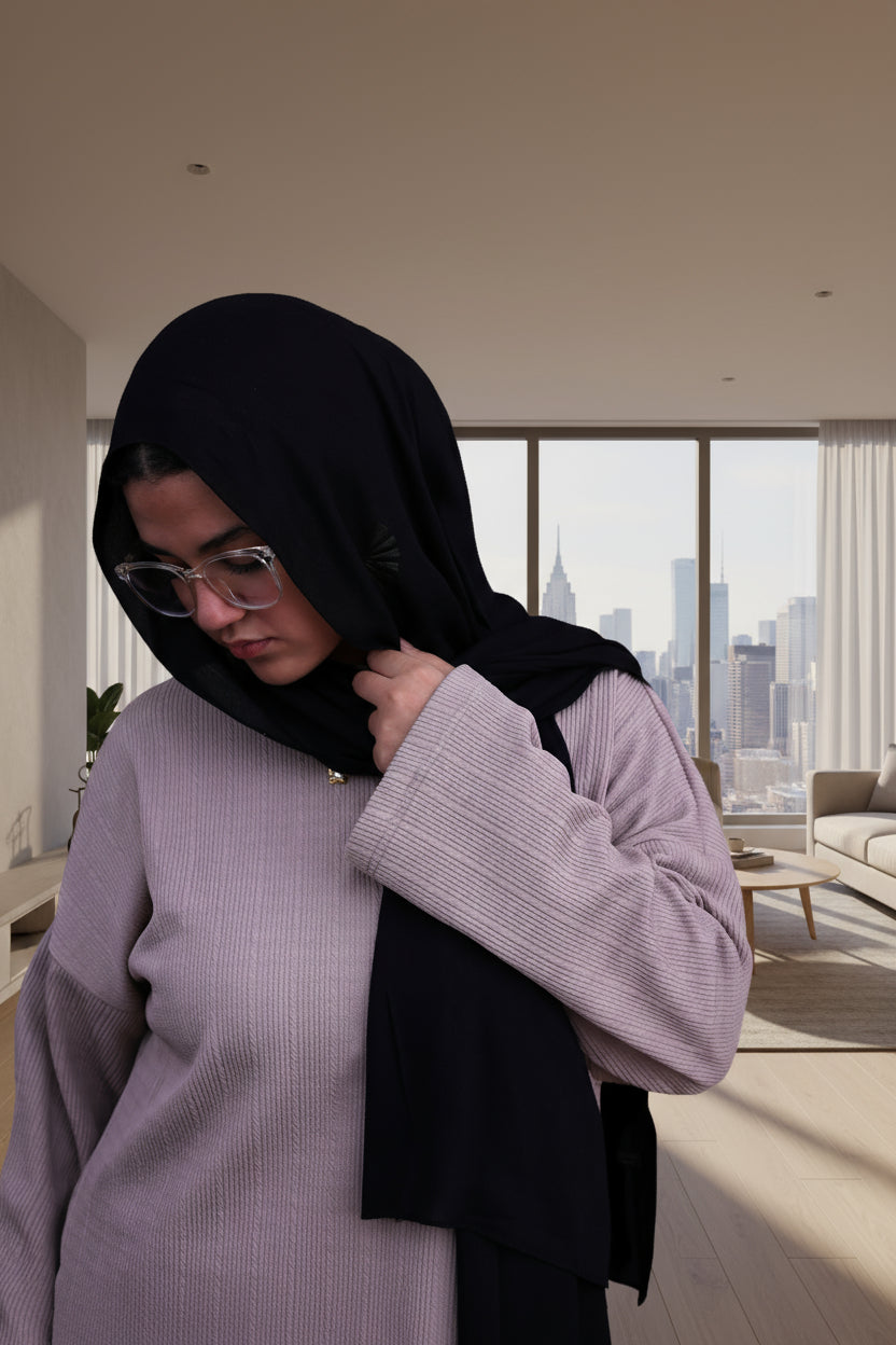 Woman wearing a black hijab and cafe outfit against a black background