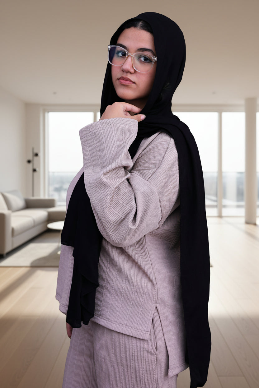 Woman wearing a black hijab and cafe outfit against a black background