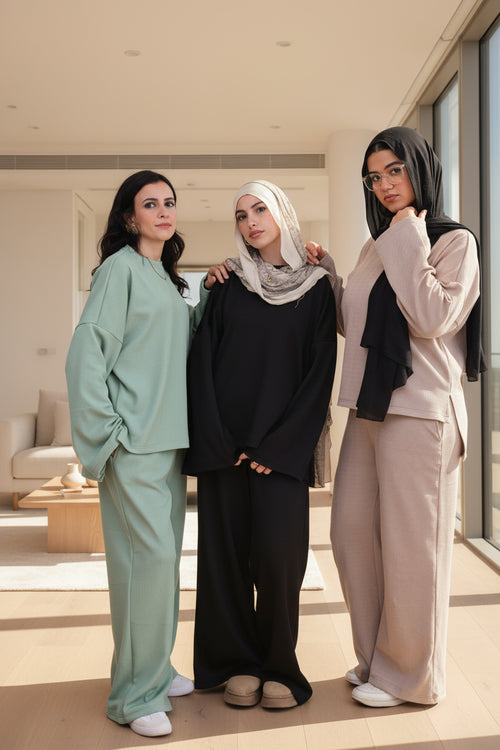 Three women wearing hijabs and casual outfits against a black background