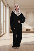 Person wearing a black outfit with a beige headscarf on a white background