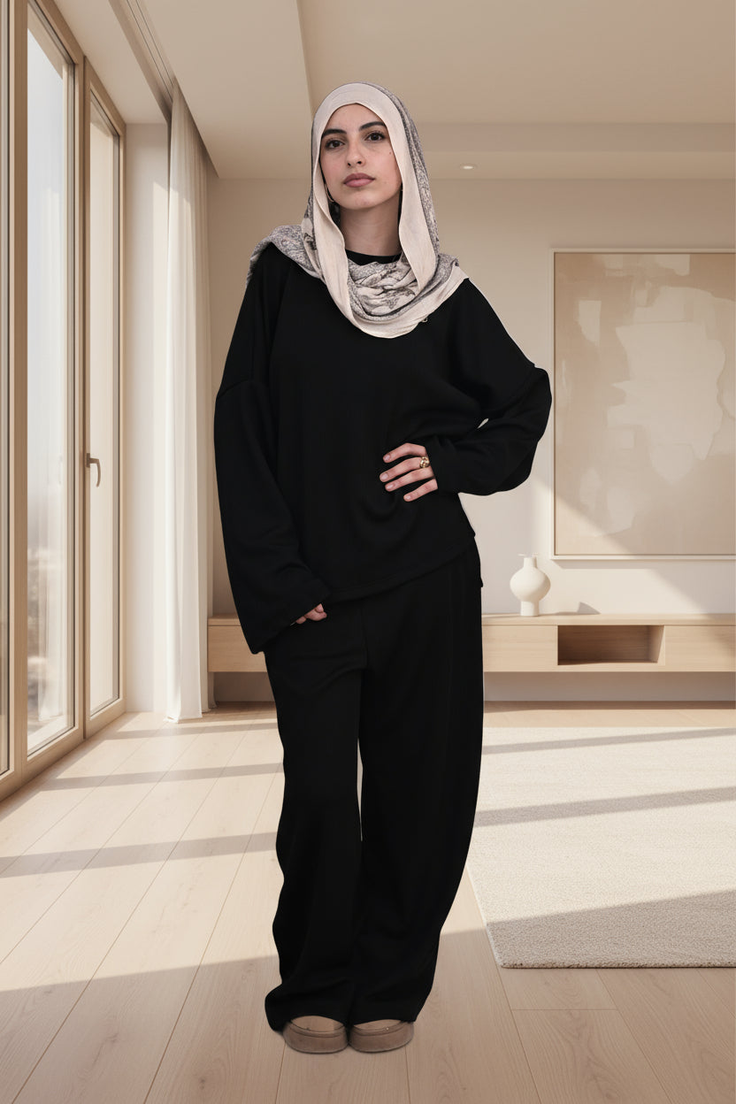 Person wearing a black outfit with a beige headscarf on a white background