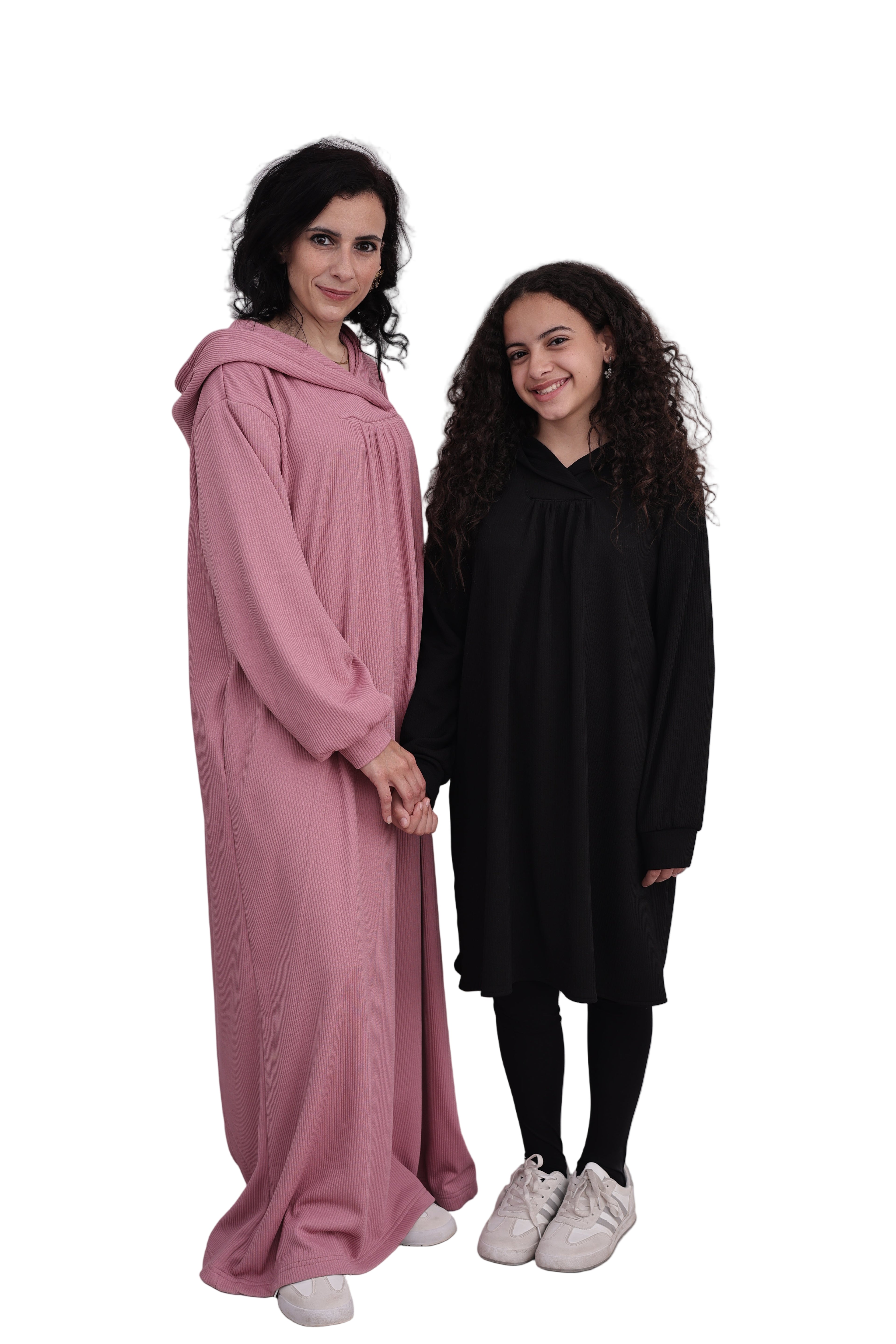 Two women standing side by side on a plain background, one in a pink dress and the other in black.